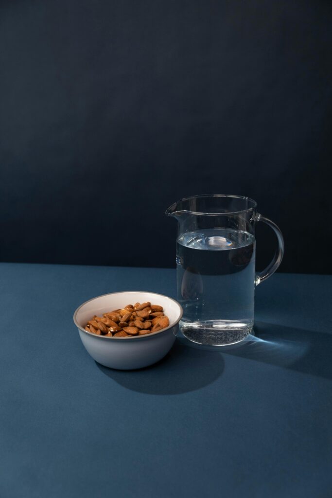 A ceramic bowl with almonds and a glass pitcher of water against a dark blue background.