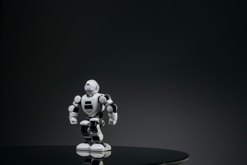 A small white robot stands on a reflective surface in a dark studio setting, showcasing modern technology.